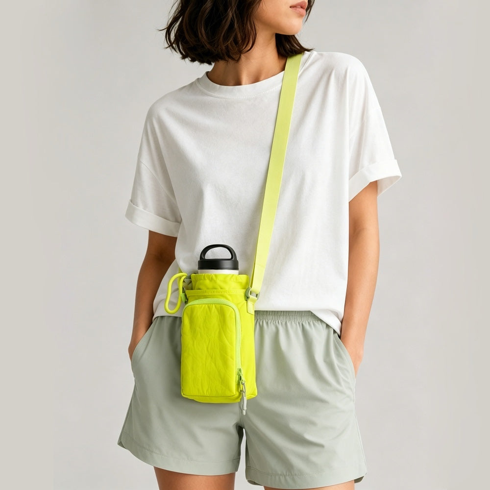 Front view of a model wearing grey shorts styling the vibrant lime green nylon bottle sling bag across the chest.