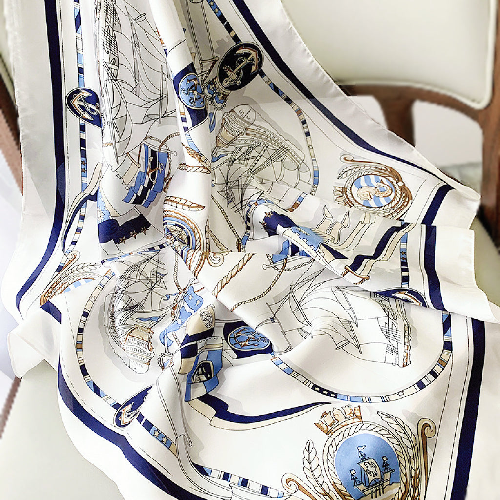 Flat lay of a White satin square scarf with blue nautical chart design, ships, and anchors in navy.