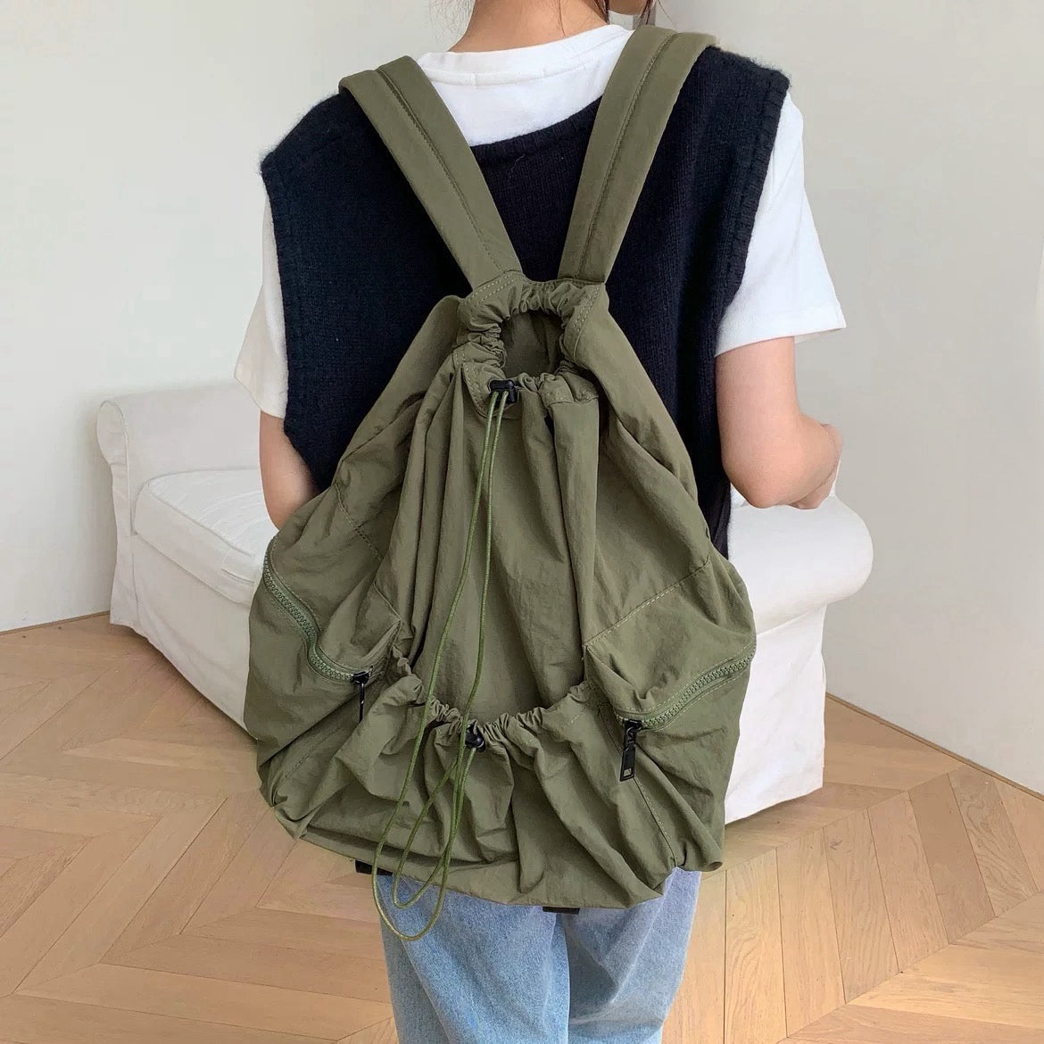 Model wearing olive green waterproof polyester backpack with drawstring closure and functional side zip pockets.