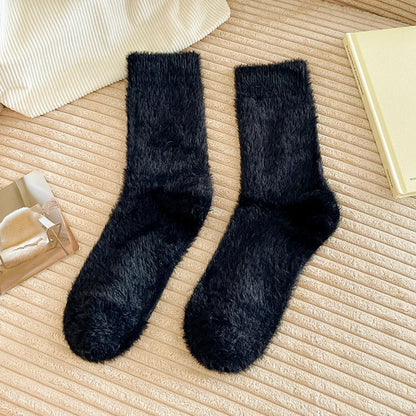 Angled view of black plush cozy socks on a textured beige surface.