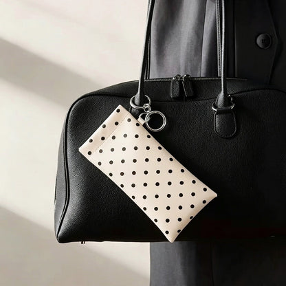 Cream white polka dot glasses clipped onto the exterior handle of a black leather handbag using its metal ring.
