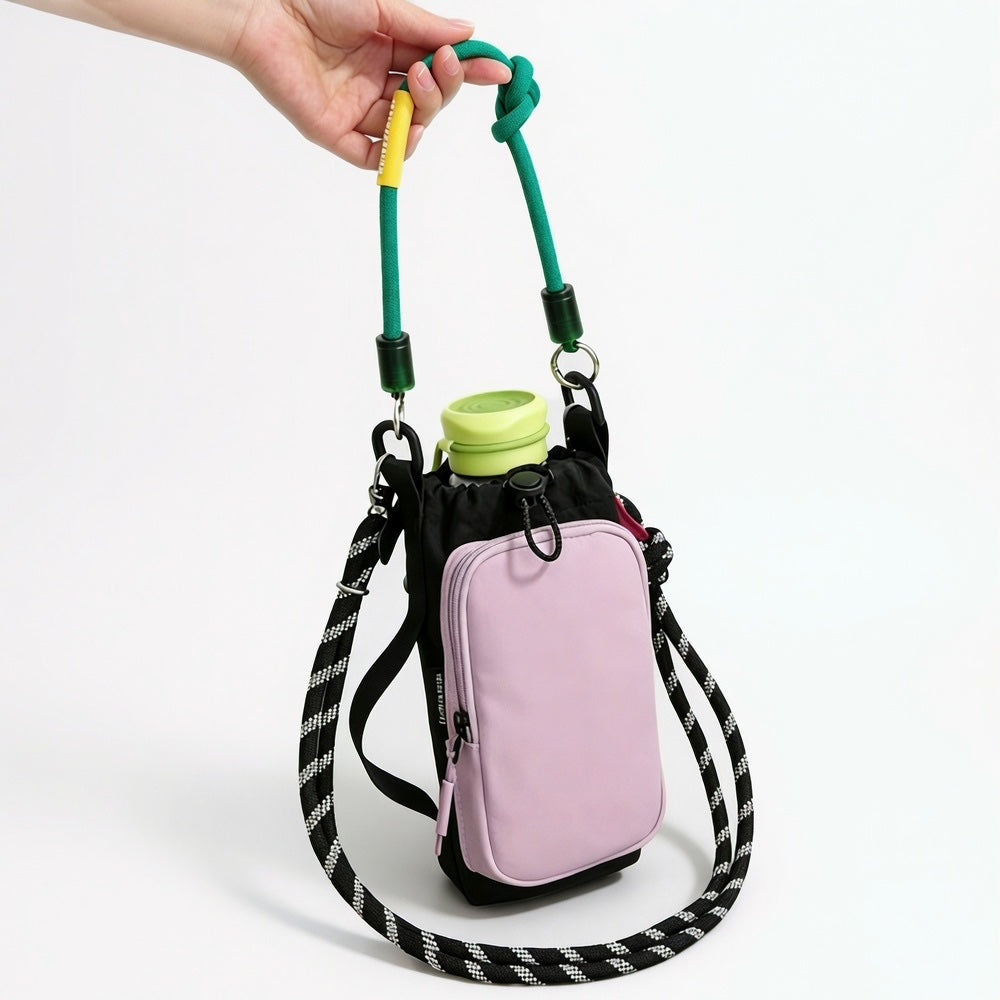 A hand holding the green contrast utility rope handle of the pastel pink water bottle  bag.