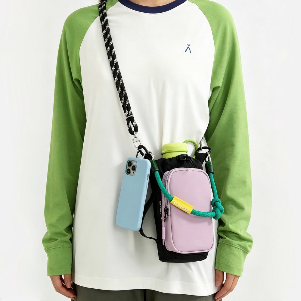 Front view of a model  styling the pastel pink utility bottle bag as a crossbody bag with a phone hanging.