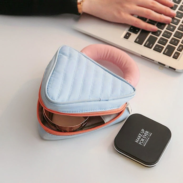 Light blue Puffy Candy triangle mini bag half-open on desk; quilted zip case for cosmetics and small tech.