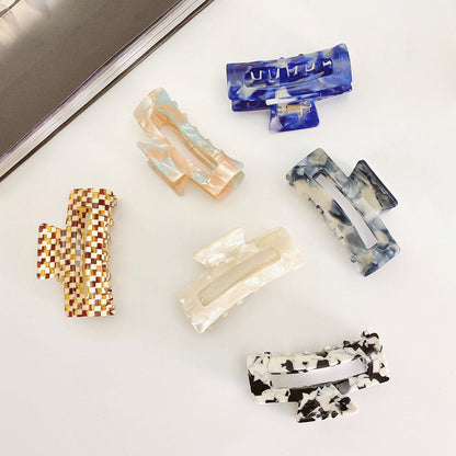 Angled view of six rectangle acrylic hair claws in various marbled colors.