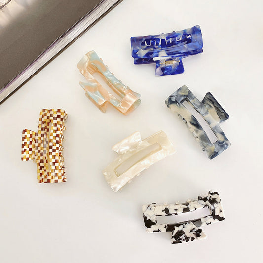 Angled view of six rectangle acrylic hair claws in various marbled colors.