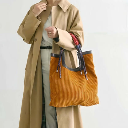 Frontal view of the reversible tote bag held as a handbag, showcasing the soft mustard corduroy texture and braided handle.