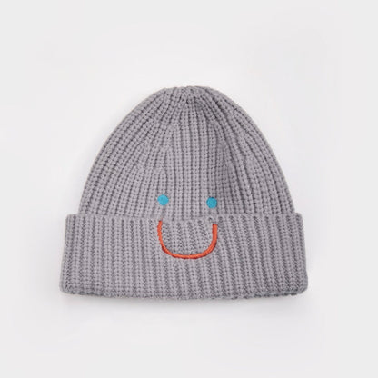 Gray ribbed knit beanie with an embroidered blue-eyed smiley face, adding a playful touch to winter gear.