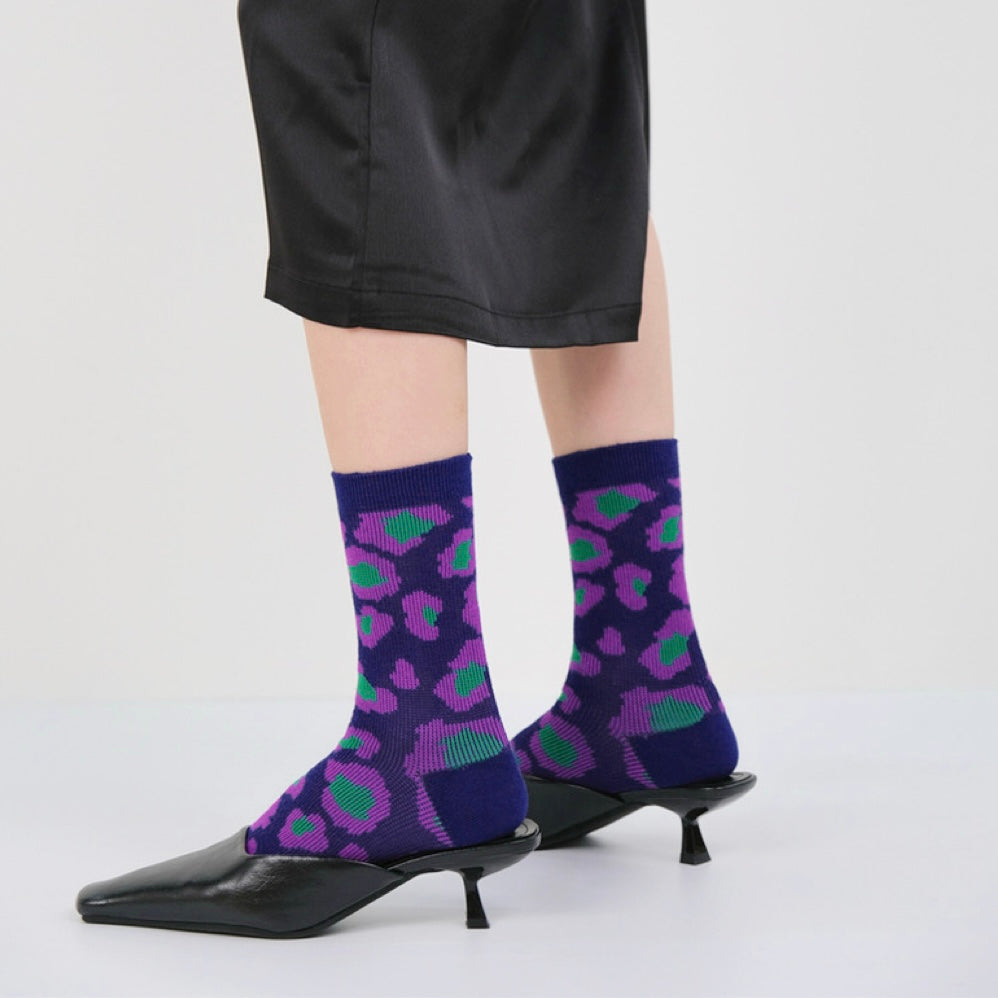 Model wearing a pair of Southern Flower Socks: Dark blue socks with purple and green abstract floral pattern.