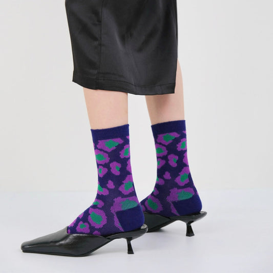 Model wearing a pair of Southern Flower Socks: Dark blue socks with purple and green abstract floral pattern.
