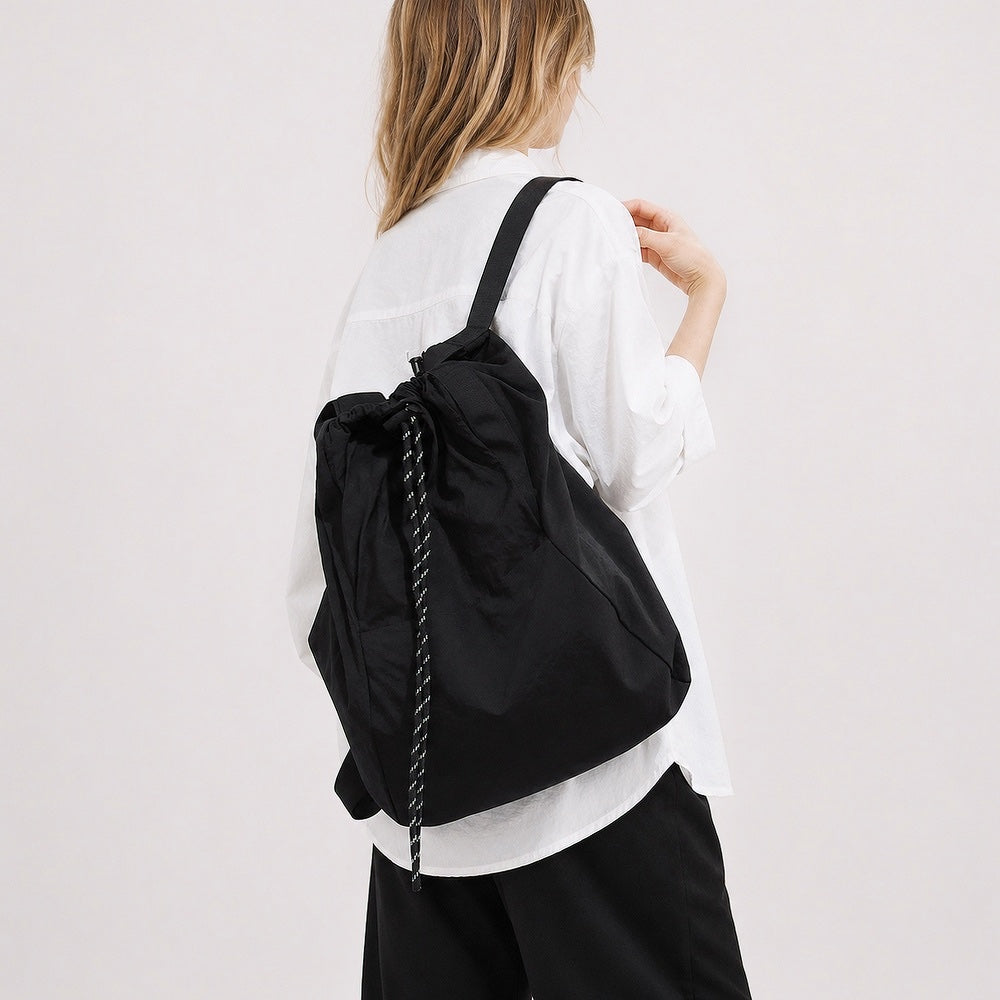 Model wearing the classic black 2-way drawstring backpack over one shoulder as a tote.