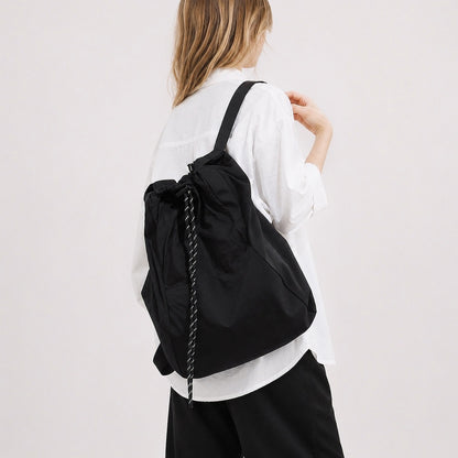 Model wearing the classic black 2-way drawstring backpack over one shoulder as a tote.