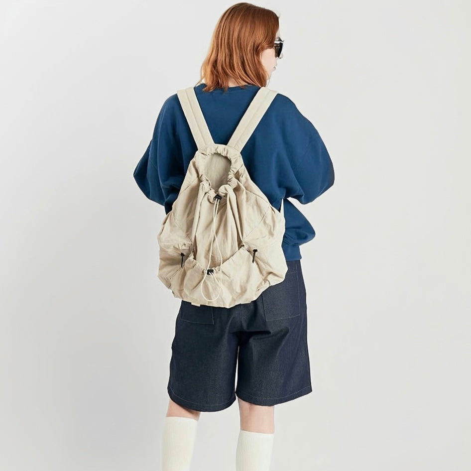 Model wearing cream backpack from behind; minimalist sporty look suited for active lifestyles and hiking.