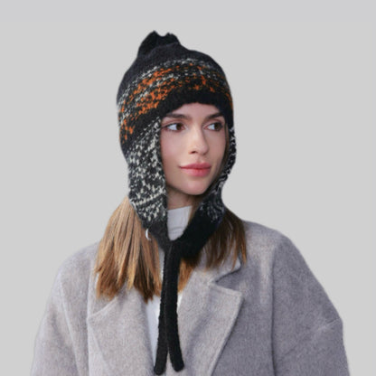 Woman wearing a black, orange, and white Winter Isle ear flap hat with secure chin ties for cold-weather protection.