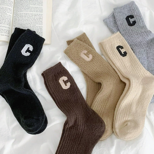 Front view of Five pairs of wool crew socks in black, brown, tan, beige, and grey, each with a white or black C.